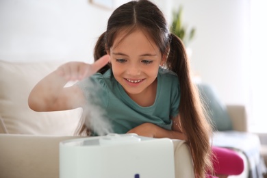 Photo of Little girl near modern air humidifier at home