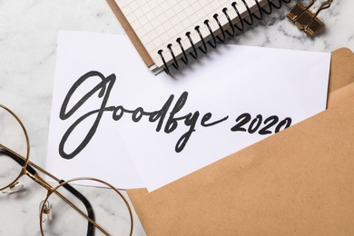 Text Goodbye 2020 written on sheet of paper on white marble table, flat lay