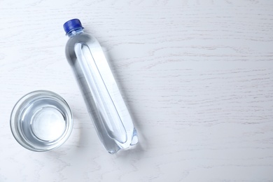 Photo of Glass and plastic bottle with water on white wooden background, flat lay. Space for text