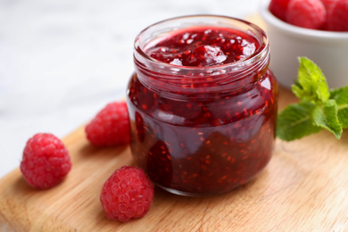 Photo of Delicious jam and fresh raspberries on wooden board, closeup