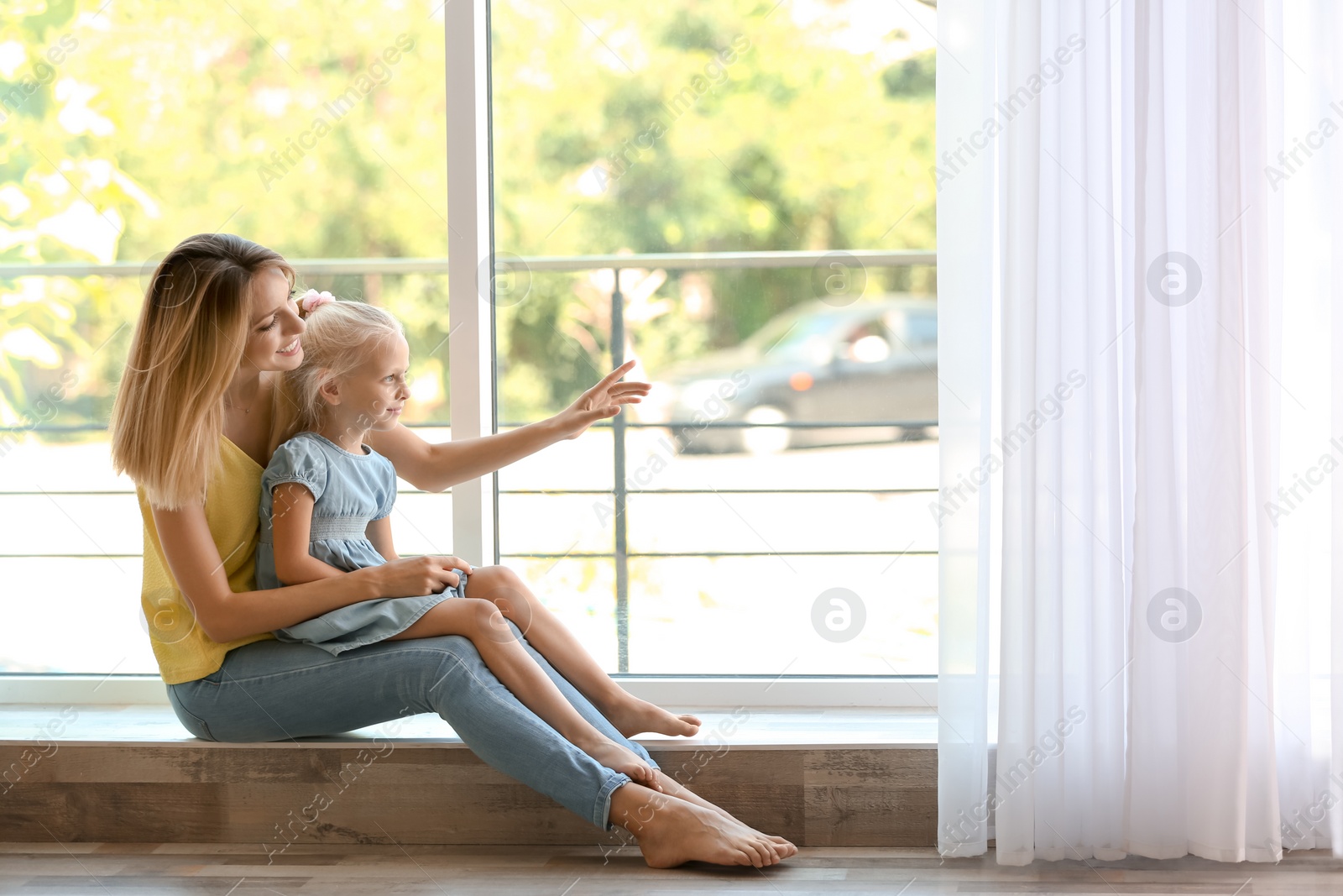 Photo of Young woman with cute little girl near window at home