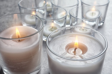 Photo of Burning wax candles in glasses on table, closeup