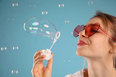 Young woman blowing soap bubbles on light blue background, closeup. Space for text