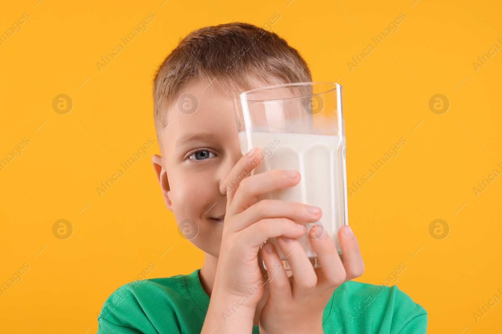 Photo of Cute boy with glass of fresh milk on orange background