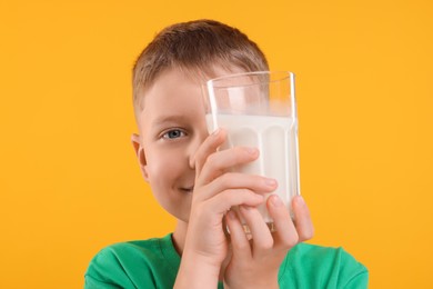 Cute boy with glass of fresh milk on orange background