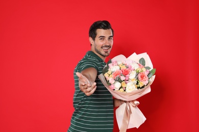 Young handsome man with beautiful flower bouquet on red background