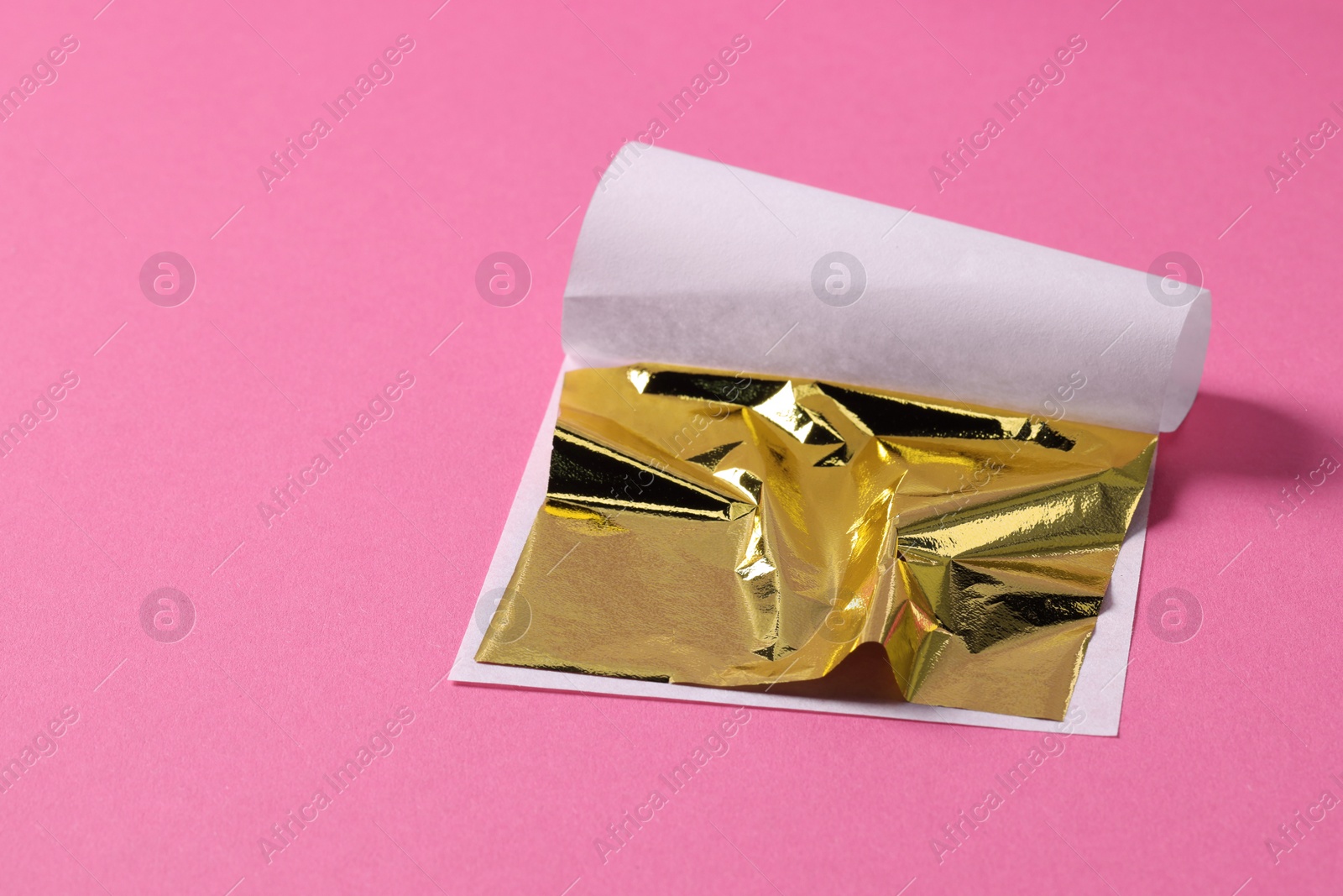 Photo of Edible gold leaf sheet on pink background, closeup. Space for text