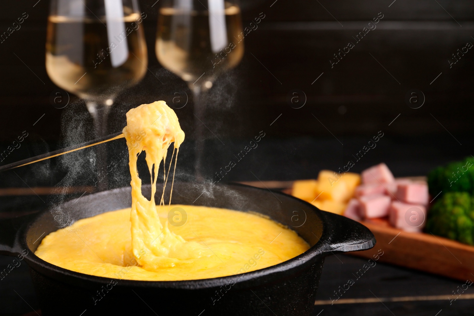 Image of Dipping piece of bread into fondue pot with tasty melted cheese at table, closeup