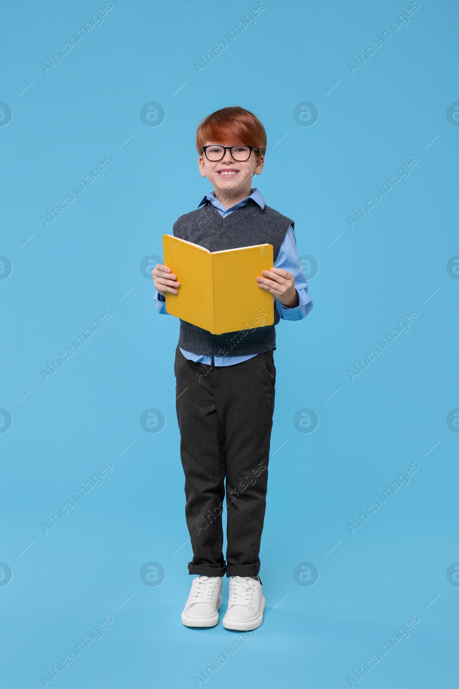 Photo of Smiling schoolboy in glasses with book on light blue background