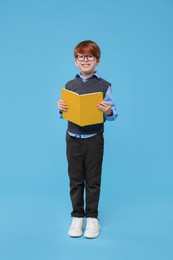Photo of Smiling schoolboy in glasses with book on light blue background