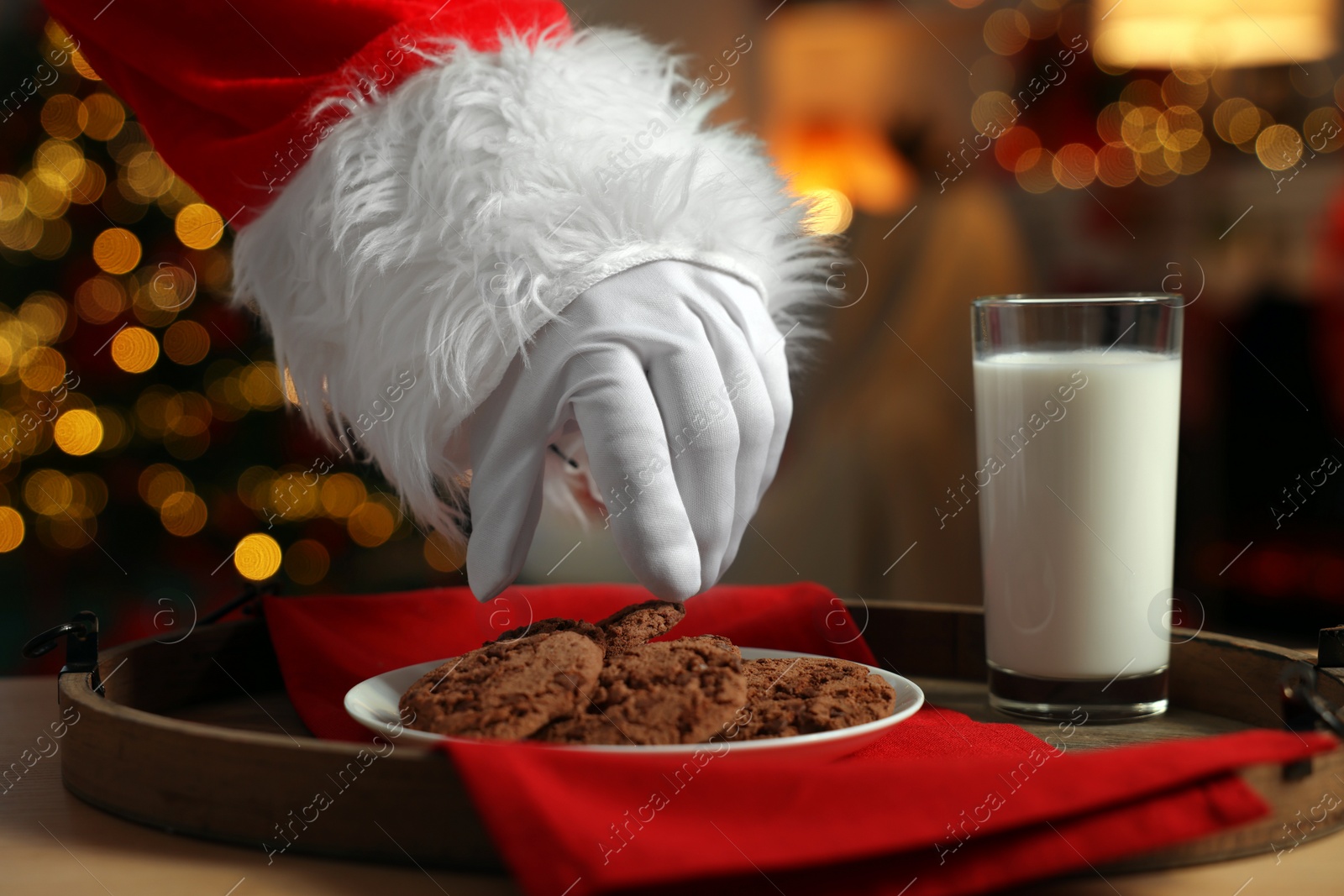 Photo of Merry Christmas. Santa Claus taking cookies from plate on table in room, closeup