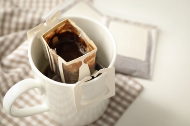 Photo of Cup with drip coffee bag on white table, closeup