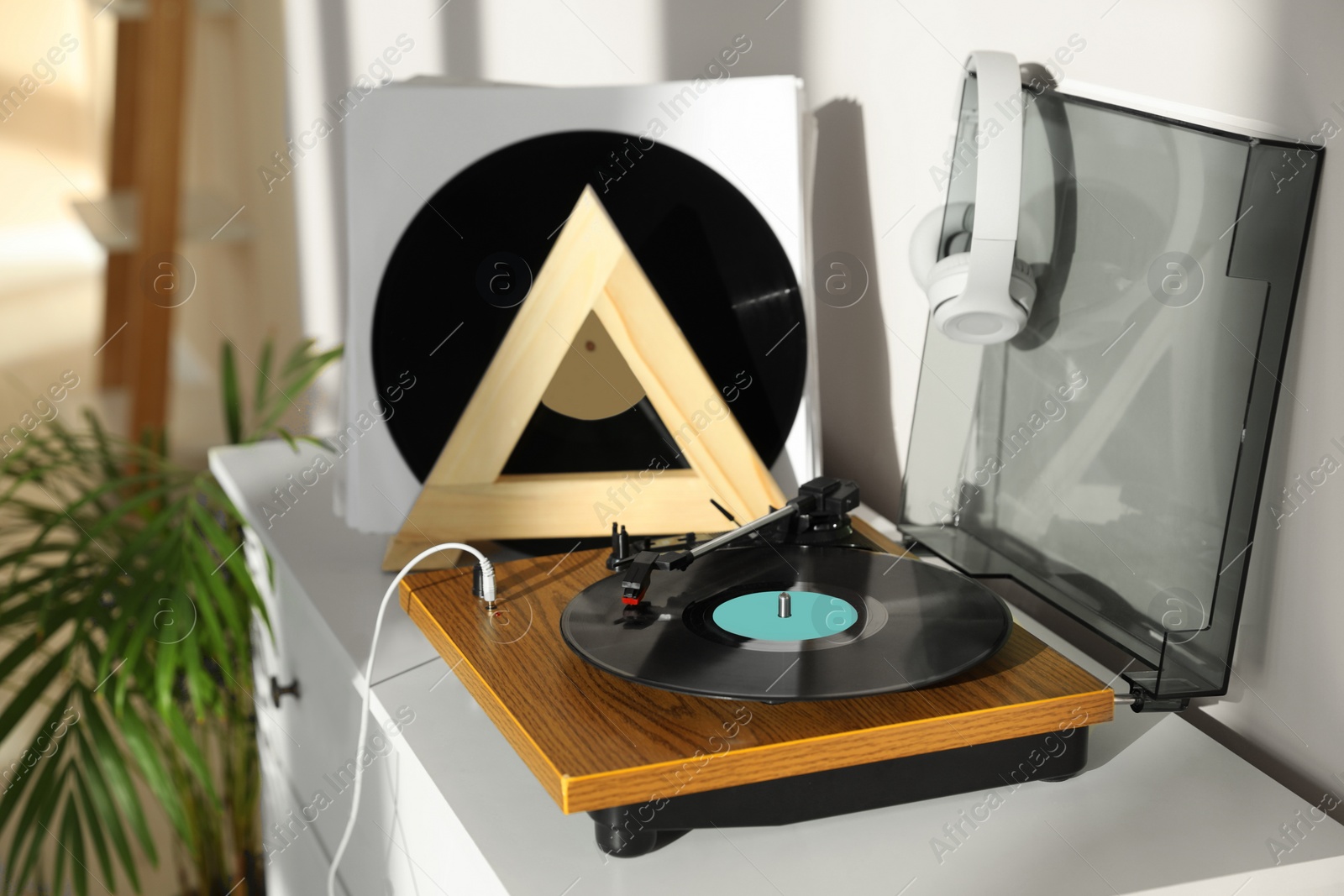 Photo of Stylish turntable with vinyl disc and headphones on white chest of drawers at home