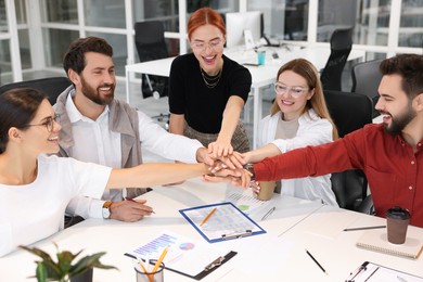 Photo of Team of employees joining hands in office