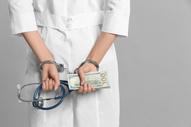 Doctor in handcuffs with bribe and stethoscope on grey background, closeup. Corrupted medicine
