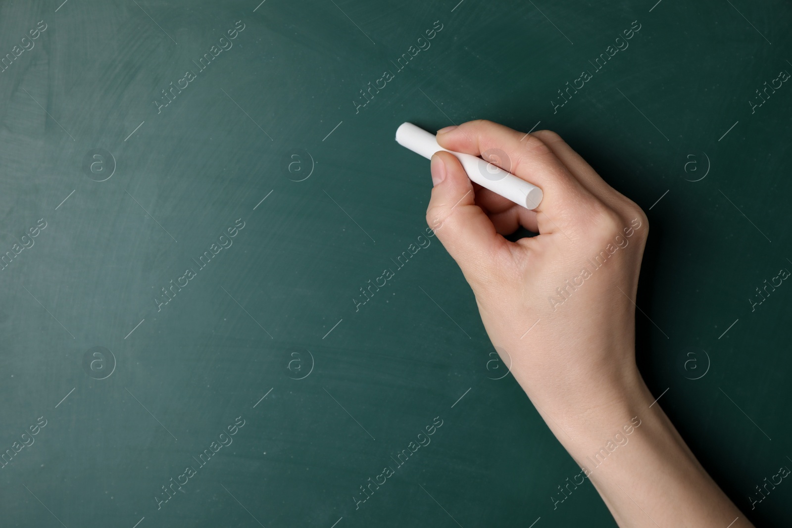 Photo of Woman with white chalk near green blackboard, closeup. Space for text