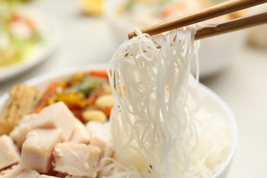 Chopsticks with tasty cooked rice noodles over bowl, closeup