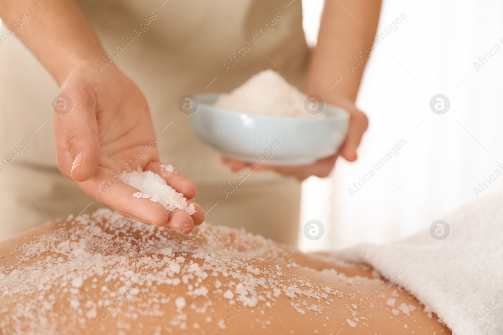 Photo of Young woman having body scrubbing procedure with sea salt in spa salon, closeup