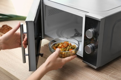 Photo of Young woman using microwave oven on table in kitchen