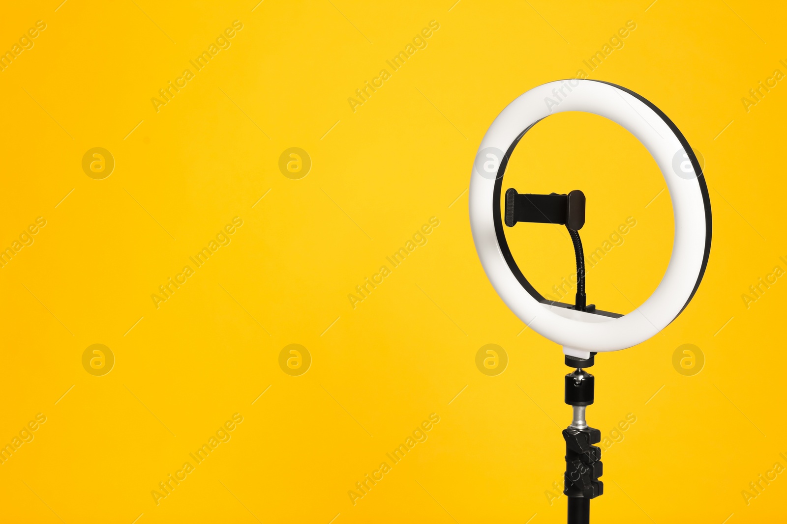 Photo of Modern tripod with ring light on yellow background. Space for text