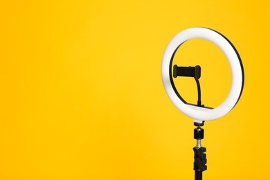 Modern tripod with ring light on yellow background. Space for text