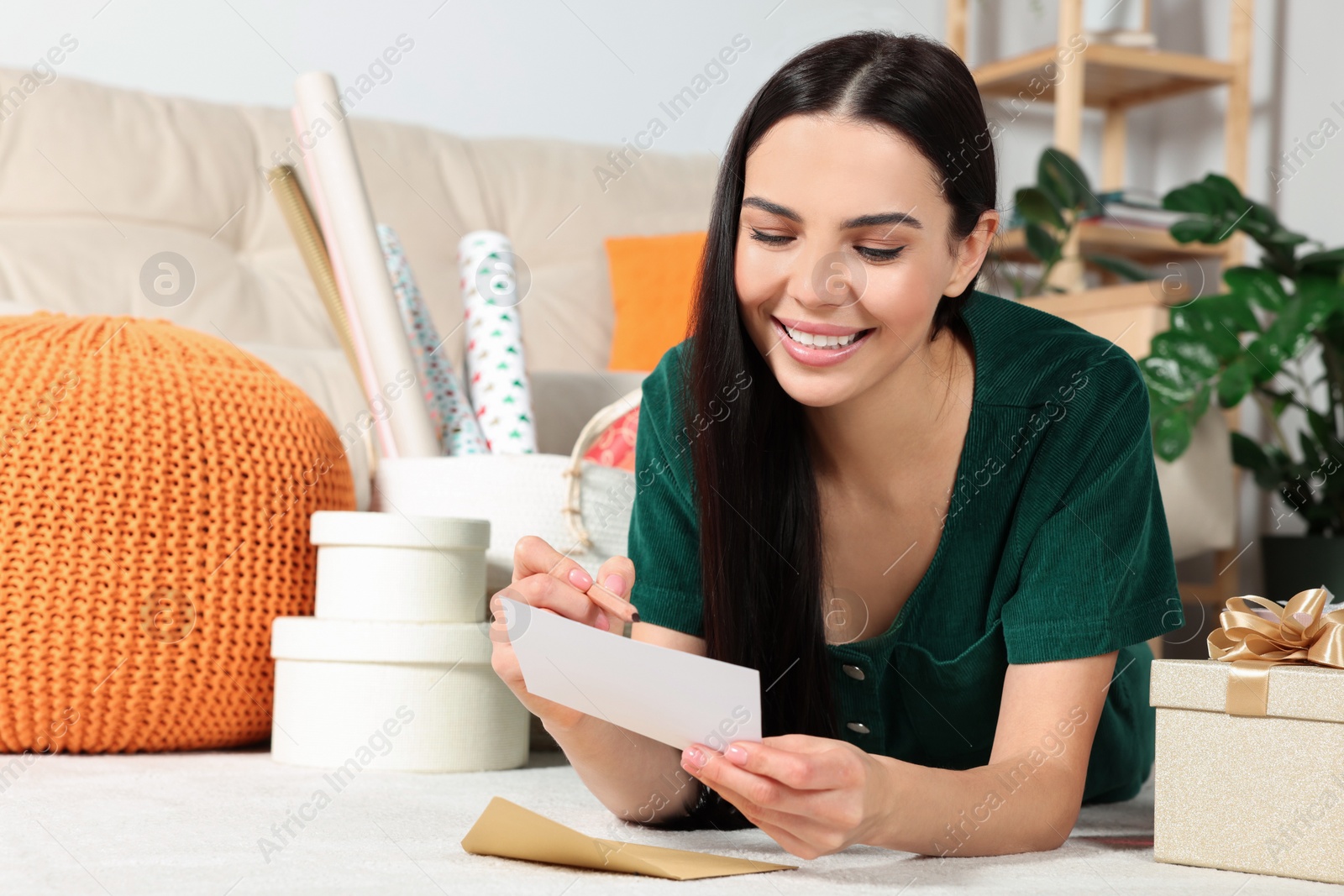 Photo of Happy woman writing message in greeting card on floor in living room