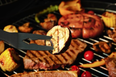 Barbecue fork with eggplant and grilled meat steaks on background