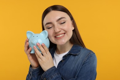 Photo of Happy woman with piggy bank on orange background