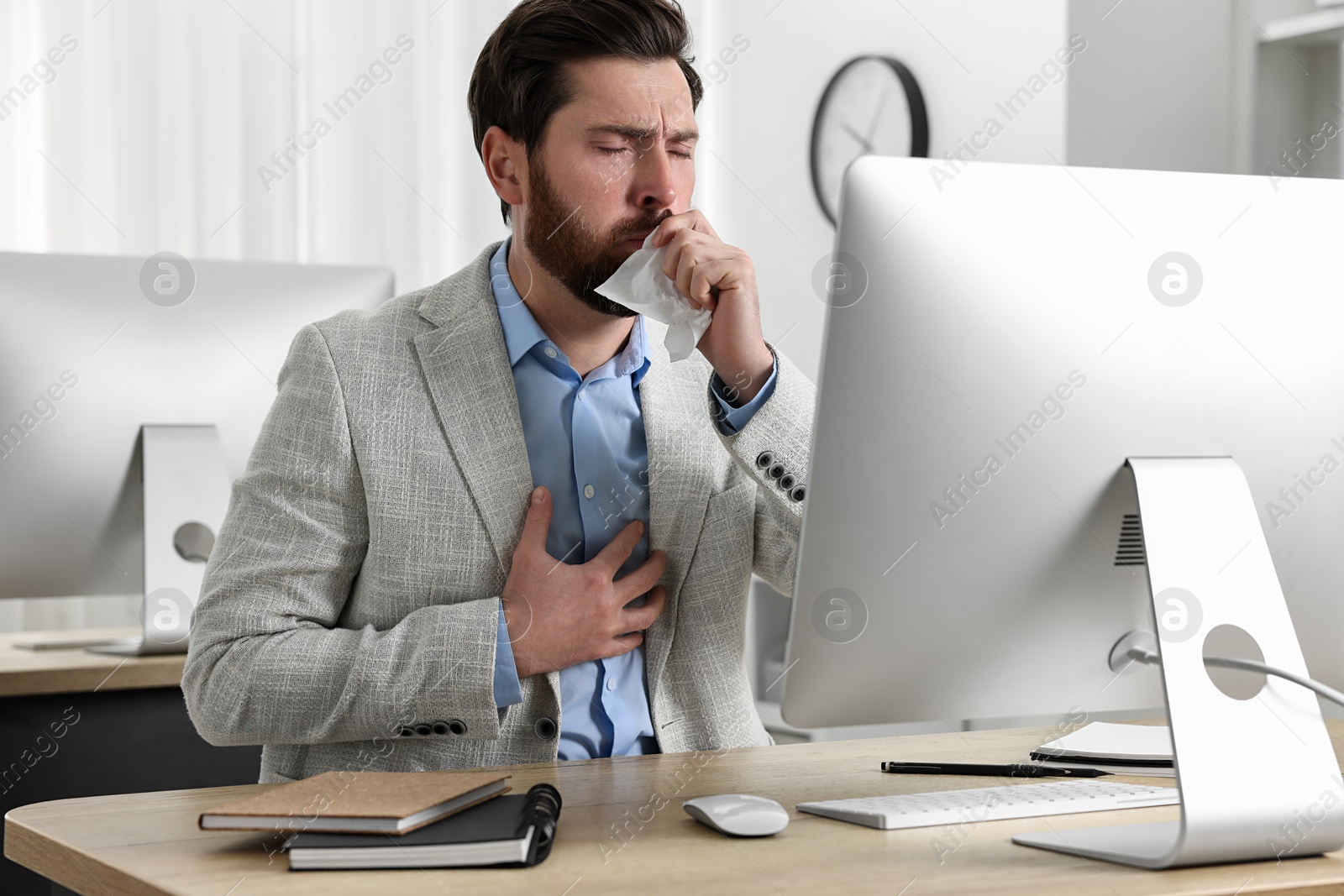 Photo of Sick man with tissue coughing at workplace in office