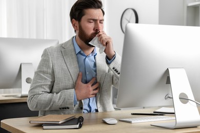 Sick man with tissue coughing at workplace in office