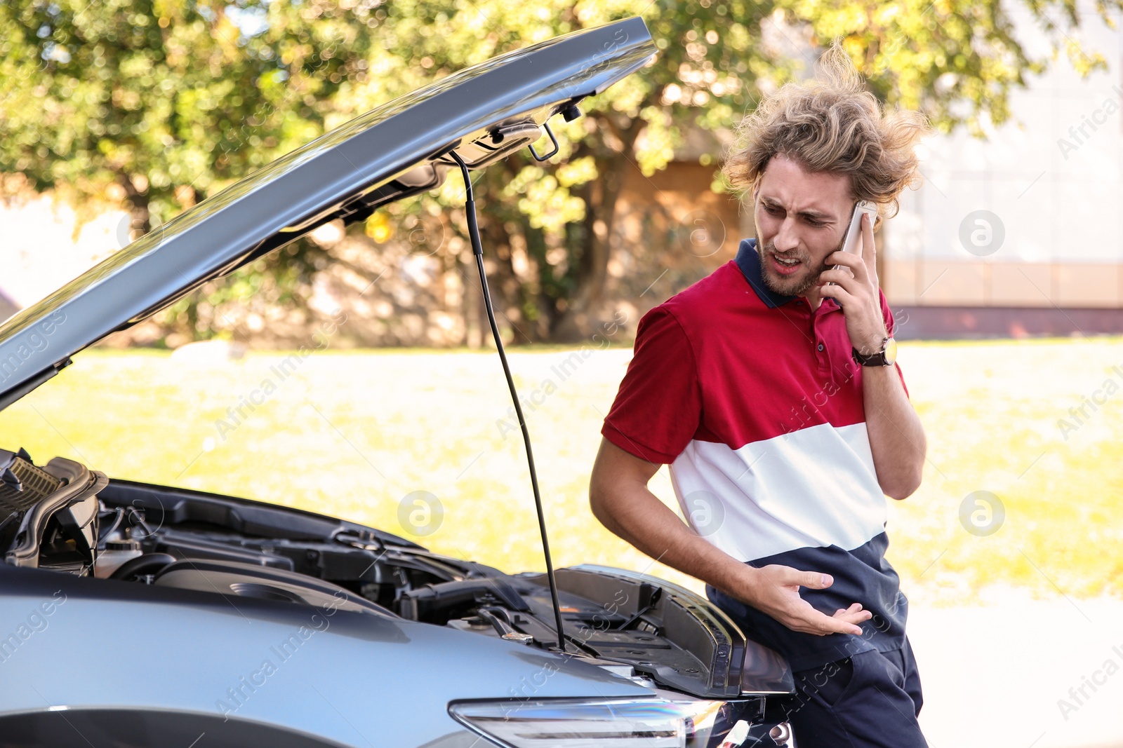 Photo of Young man talking on phone near broken car, outdoors