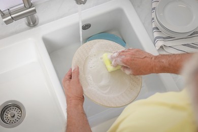 Photo of Man washing plate above sink, top view