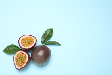 Photo of Fresh ripe passion fruits (maracuyas) with green leaves on light blue background, flat lay. Space for text