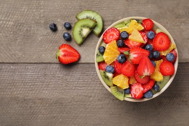 Delicious fresh fruit salad in bowl and ingredients on wooden table, flat lay. Space for text