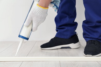 Man using caulking gun while installing plinth on laminated floor in room, closeup