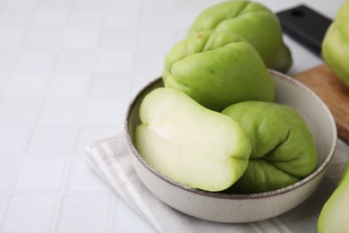 Photo of Cut and whole chayote in bowl on white tiled table, closeup. Space for text