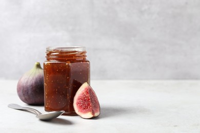 Photo of Jar of tasty sweet jam, fresh figs and spoon on white table. Space for text