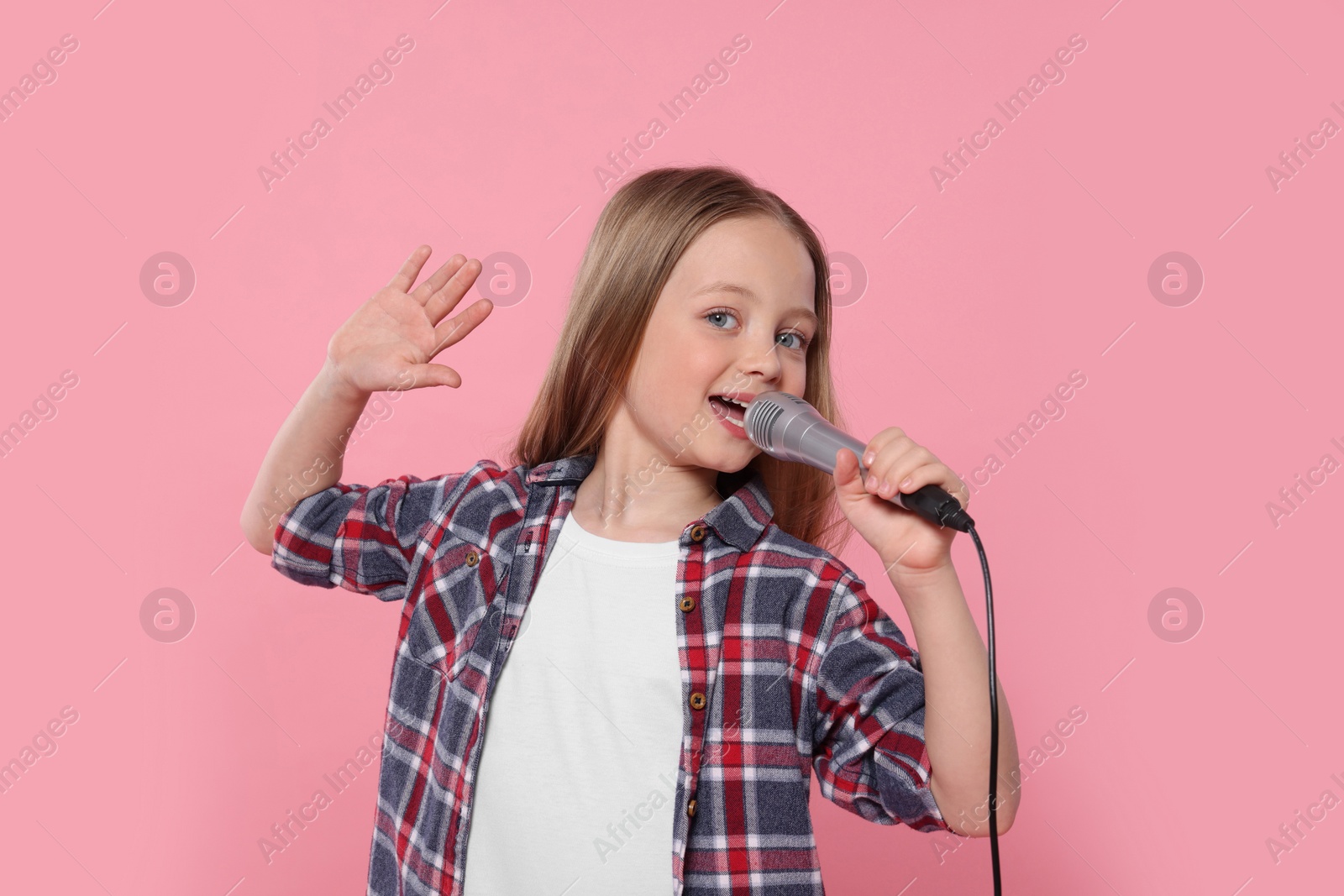 Photo of Cute little girl with microphone singing on pink background