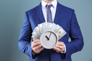 Young businessman holding clock and money on color background. Time management