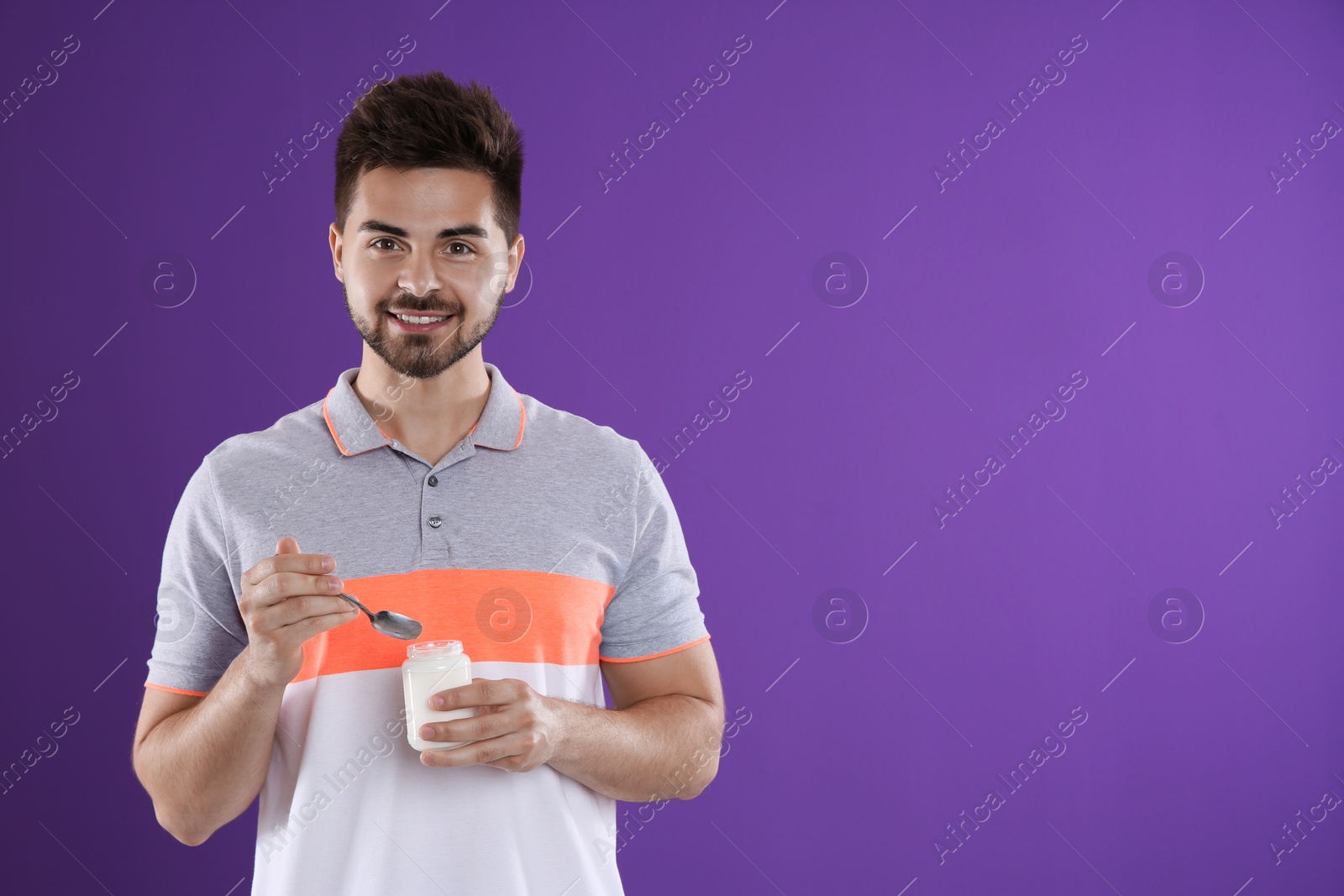 Photo of Happy young man with yogurt and spoon on purple background. Space for text