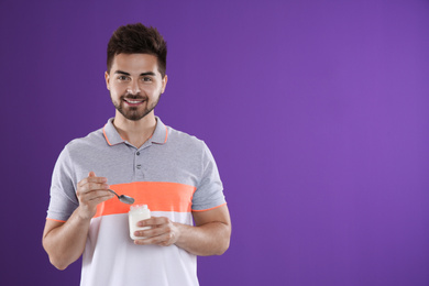 Happy young man with yogurt and spoon on purple background. Space for text