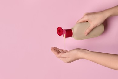 Photo of Woman pouring shampoo into palm on pink background, top view. Space for text