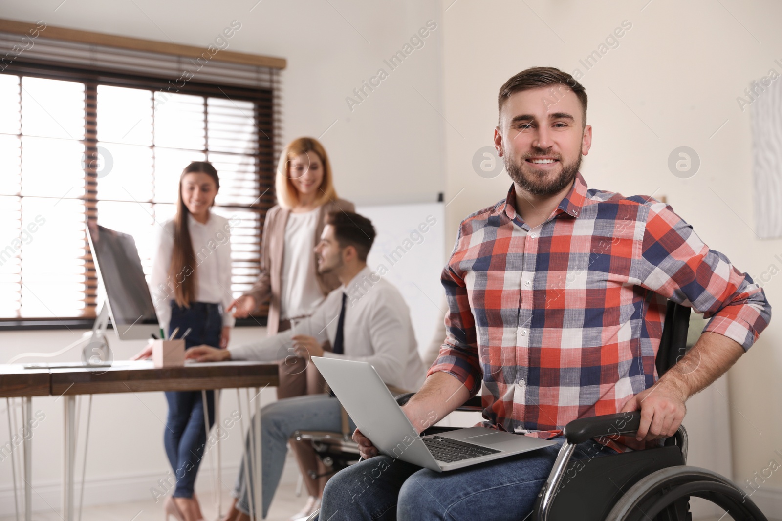 Photo of Portrait of man in wheelchair with laptop and his colleagues at workplace