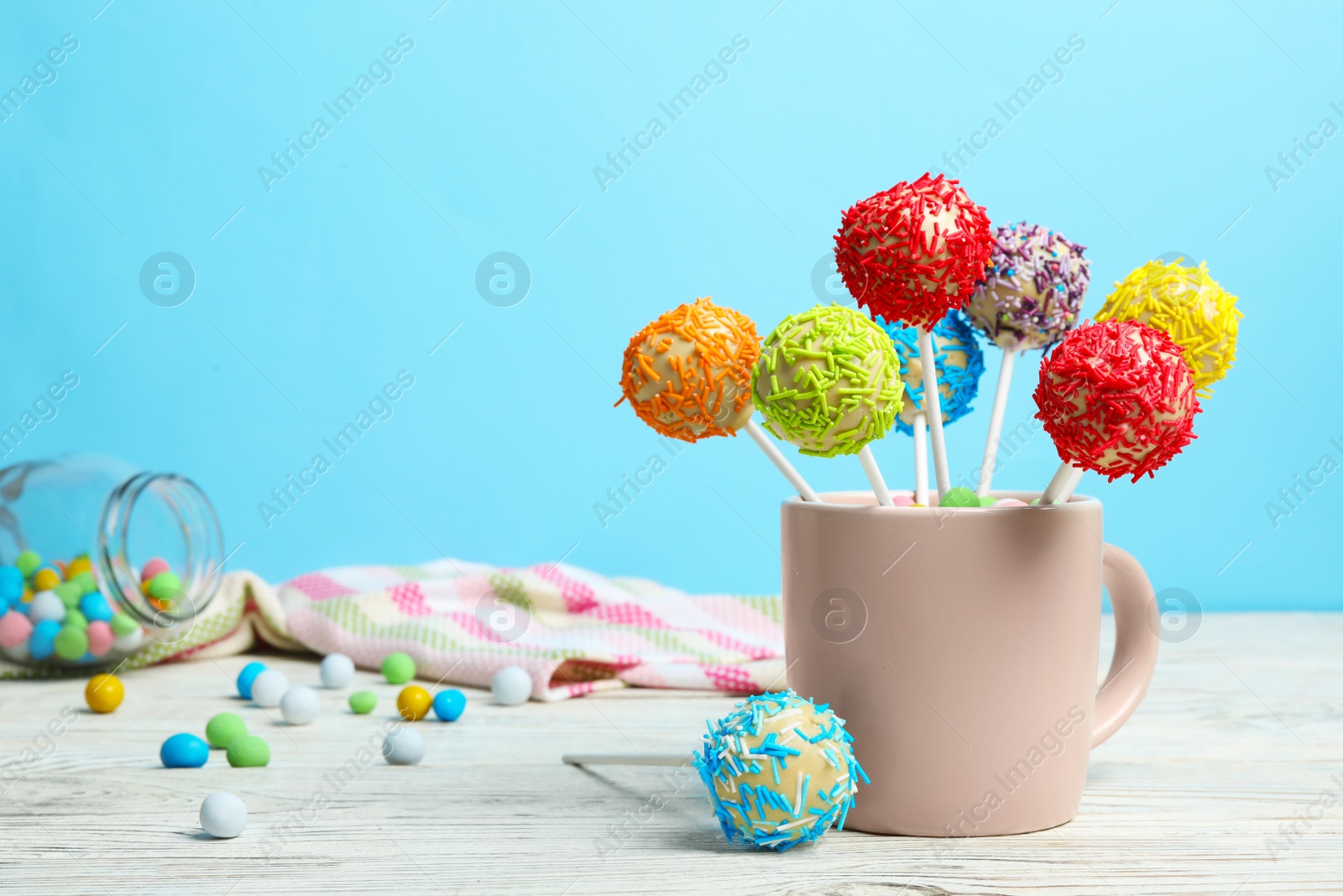 Photo of Cup with tasty cake pops on table against light blue background, space for text