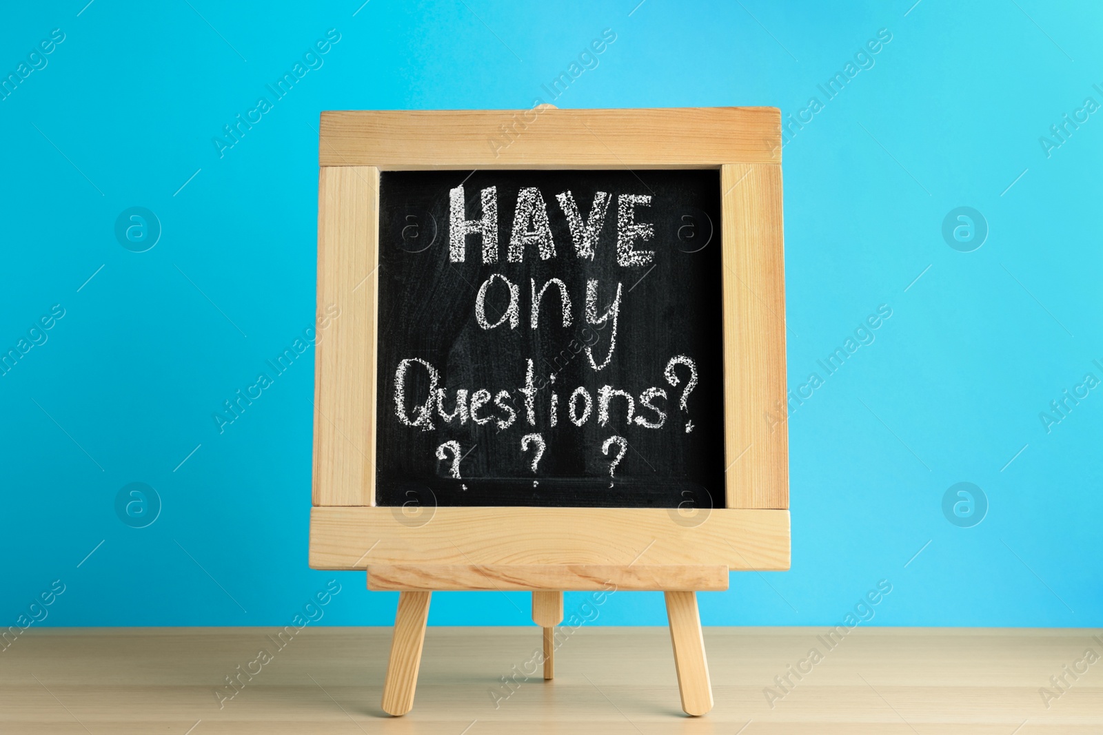Photo of Blackboard with phrase HAVE ANY QUESTIONS on wooden table against blue background