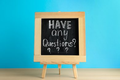 Photo of Blackboard with phrase HAVE ANY QUESTIONS on wooden table against blue background