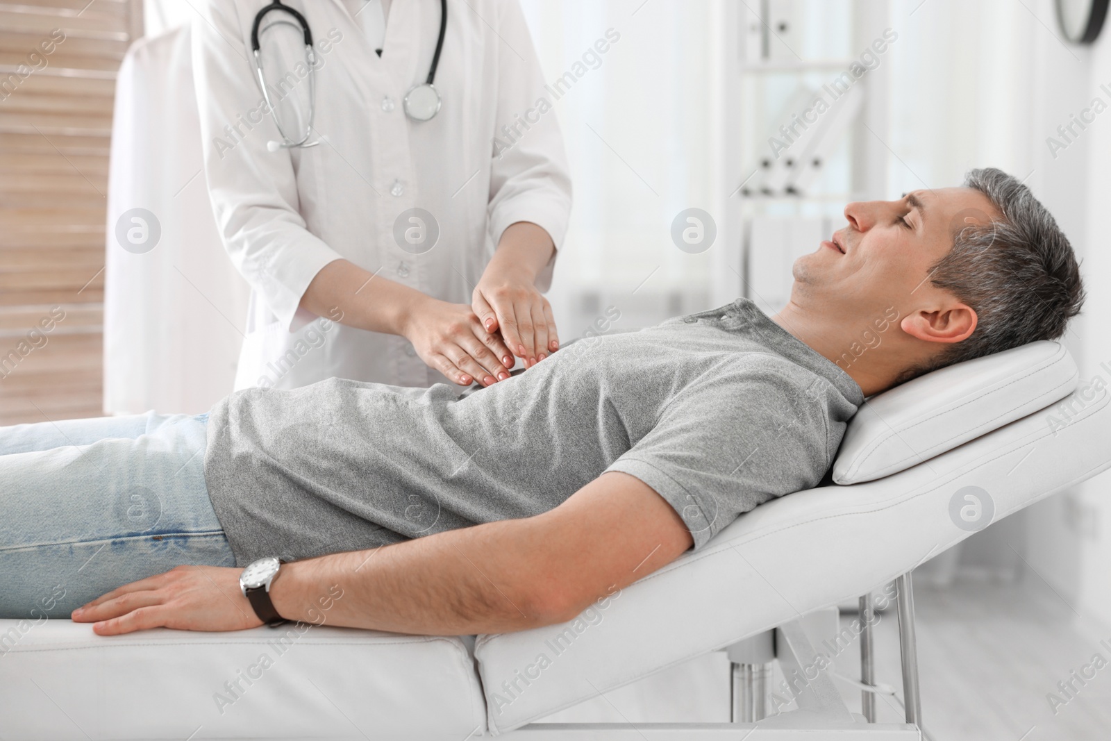 Photo of Gastroenterologist examining patient with stomach pain on couch in clinic, closeup