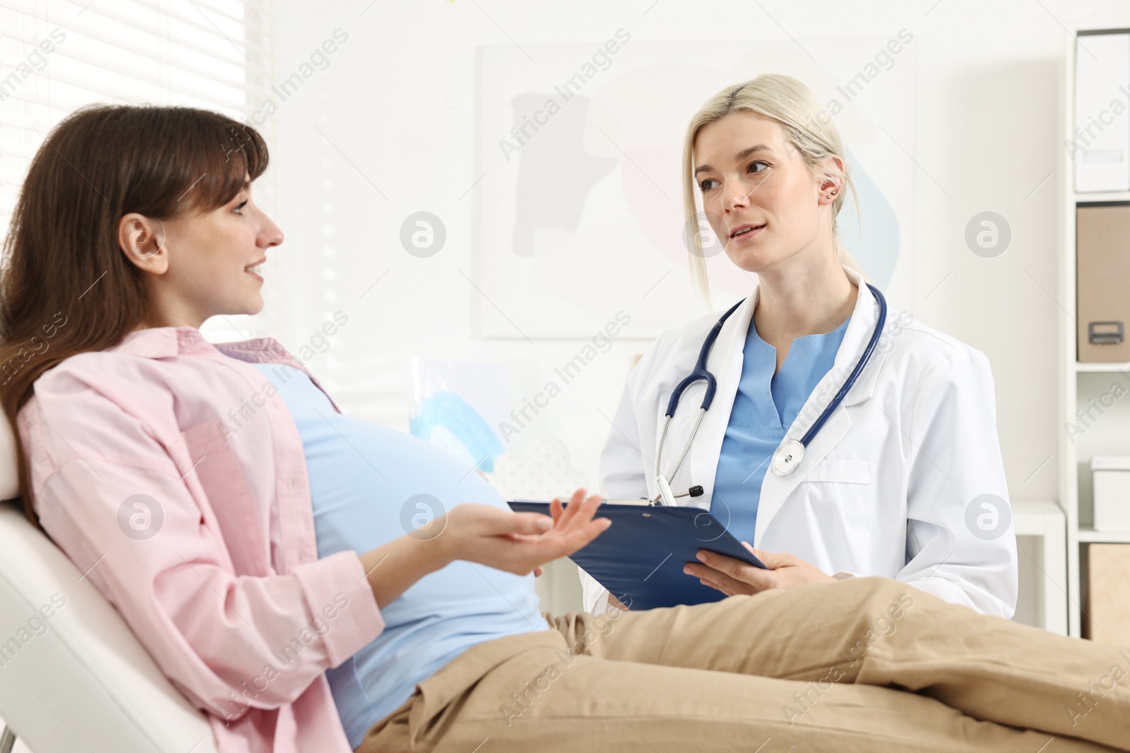 Photo of Doctor with clipboard consulting smiling pregnant patient in clinic