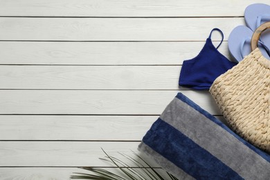 Photo of Beach towel, flip flops, straw bag and swimsuit on white wooden background, flat lay. Space for text
