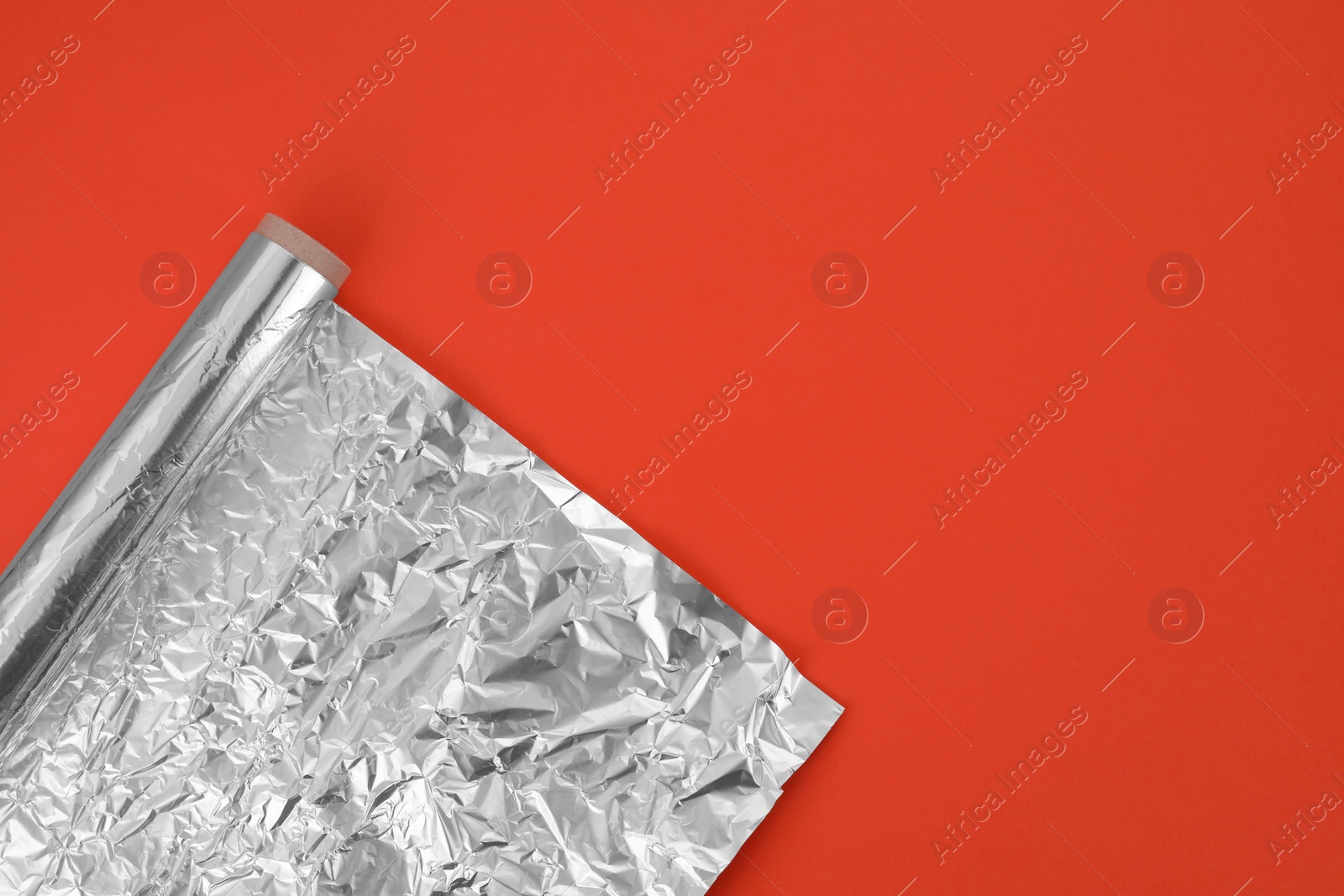 Photo of Roll of aluminum foil on orange background, top view. Space for text